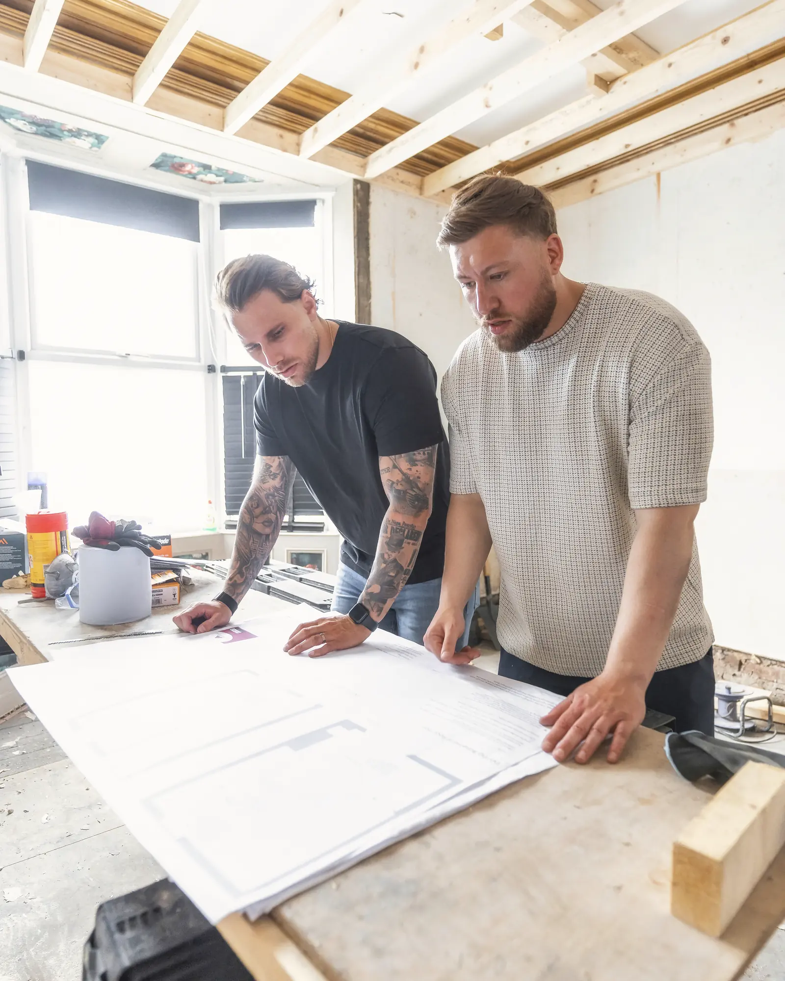 Two men leaning over large white plans in a room under construction, with exposed wooden beams. Capital One.