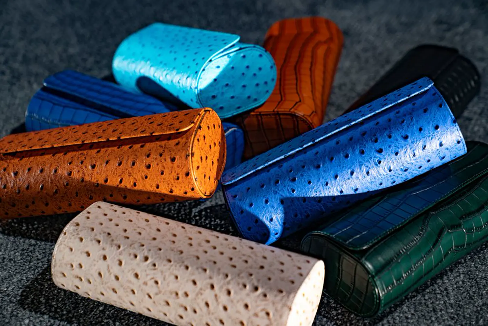A pile of rounded leather cases in cream, tan, blue, turquoise, brown, black, and green. Etier.
