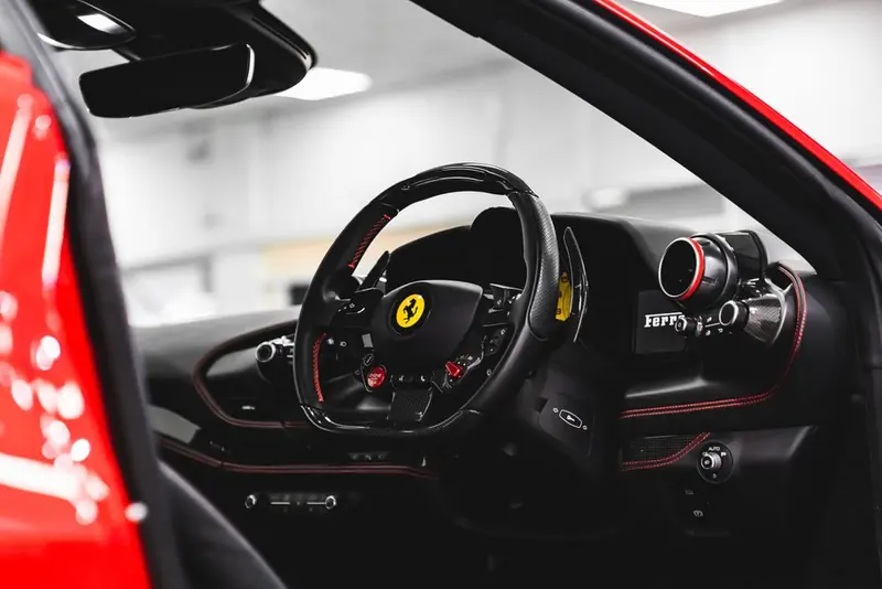 The interior of a red car in a bright showroom: a black steering wheel with red stitching and a yellow badge at the centre.