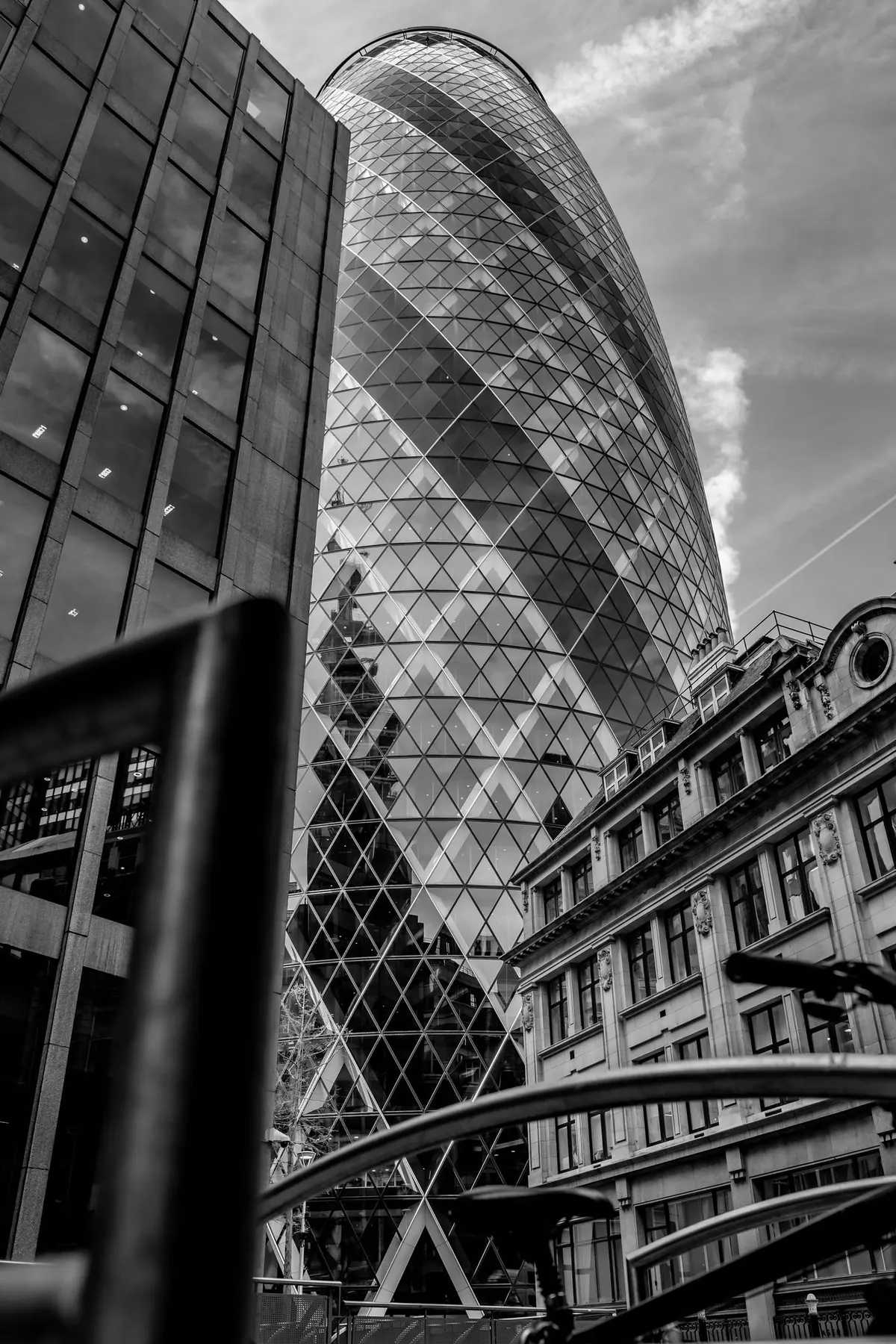Black and white photograph looking up at the Gherkin in London, the diamond glass lattice, with a blurred rail and bicycle in the foreground.