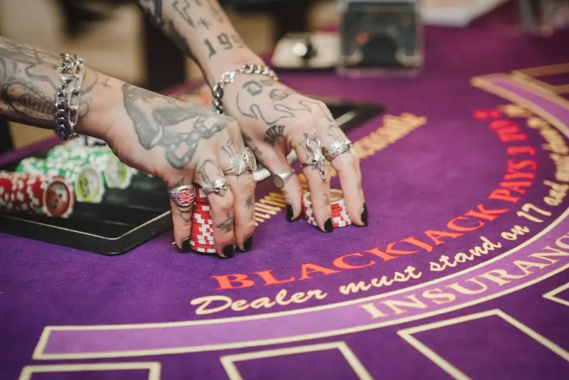 Tattooed hands with black nail polish and silver rings stacking casino chips on a purple felt table. Inn Collection Group, Newcastle.