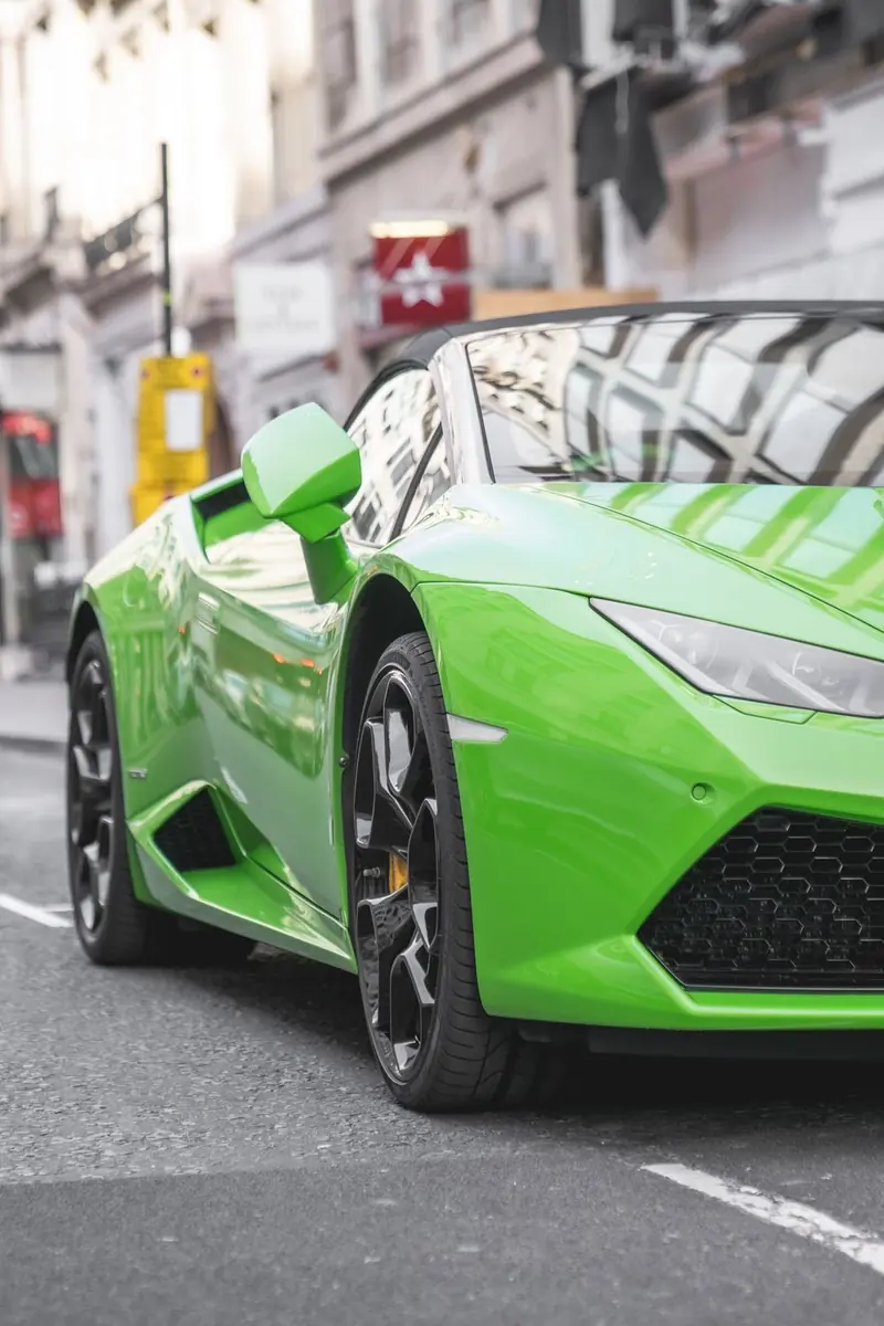 A bright green convertible sports car with black wheels, parked on a city street with white lines and buildings behind. No people.