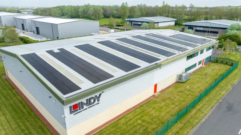 Dark solar panels covering the roof of a large grey industrial building, seen from above, with grass and a green fence. Northern Renewable Centre.