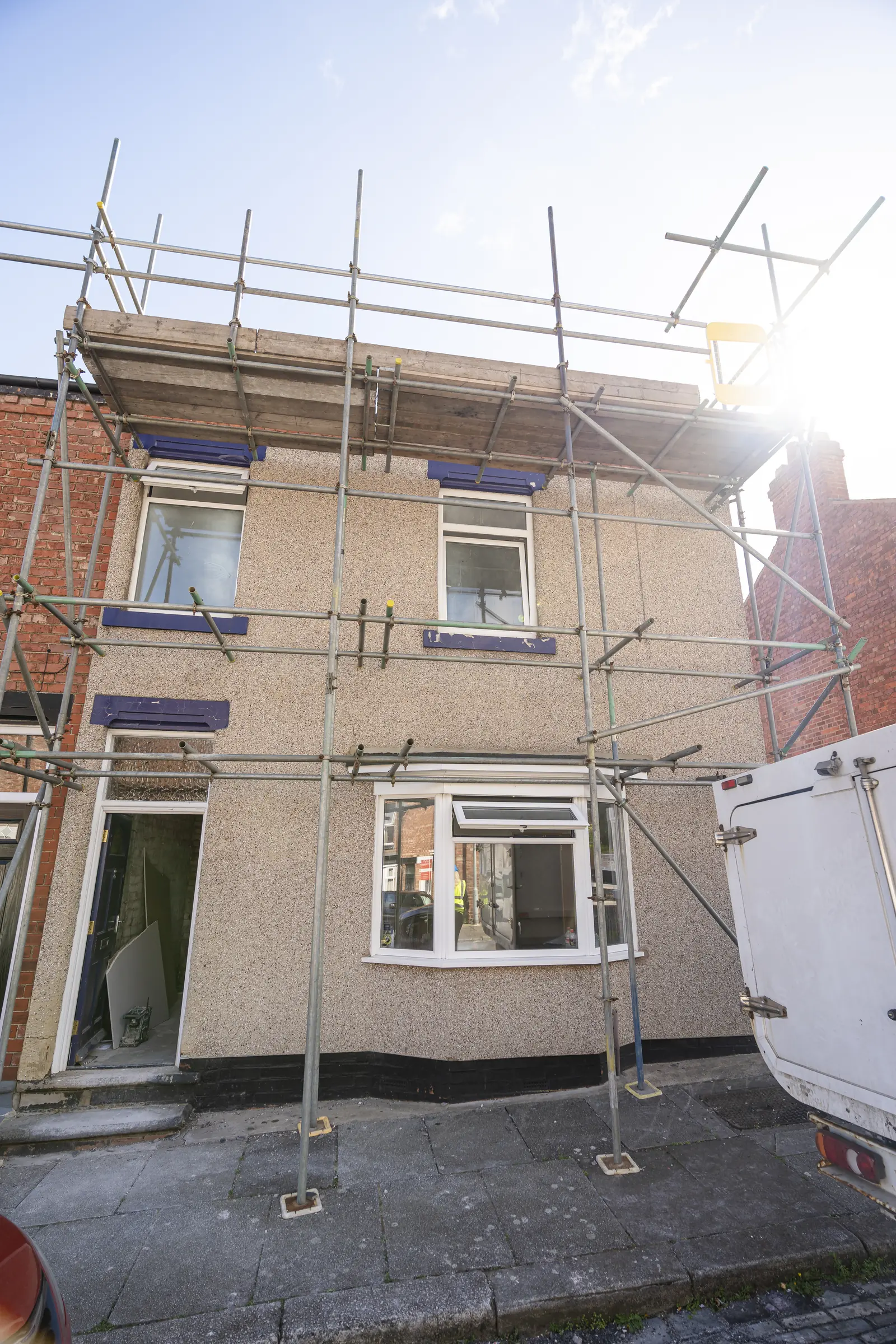 A two-storey beige house under full metal scaffolding, with a person in a yellow hi-vis jacket visible in the ground-floor window. MEL Property.