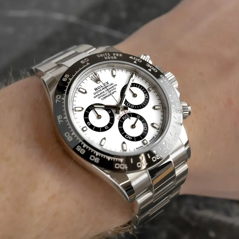 A silver chronograph with a black bezel and a white dial, worn on a wrist, against a soft grey background.