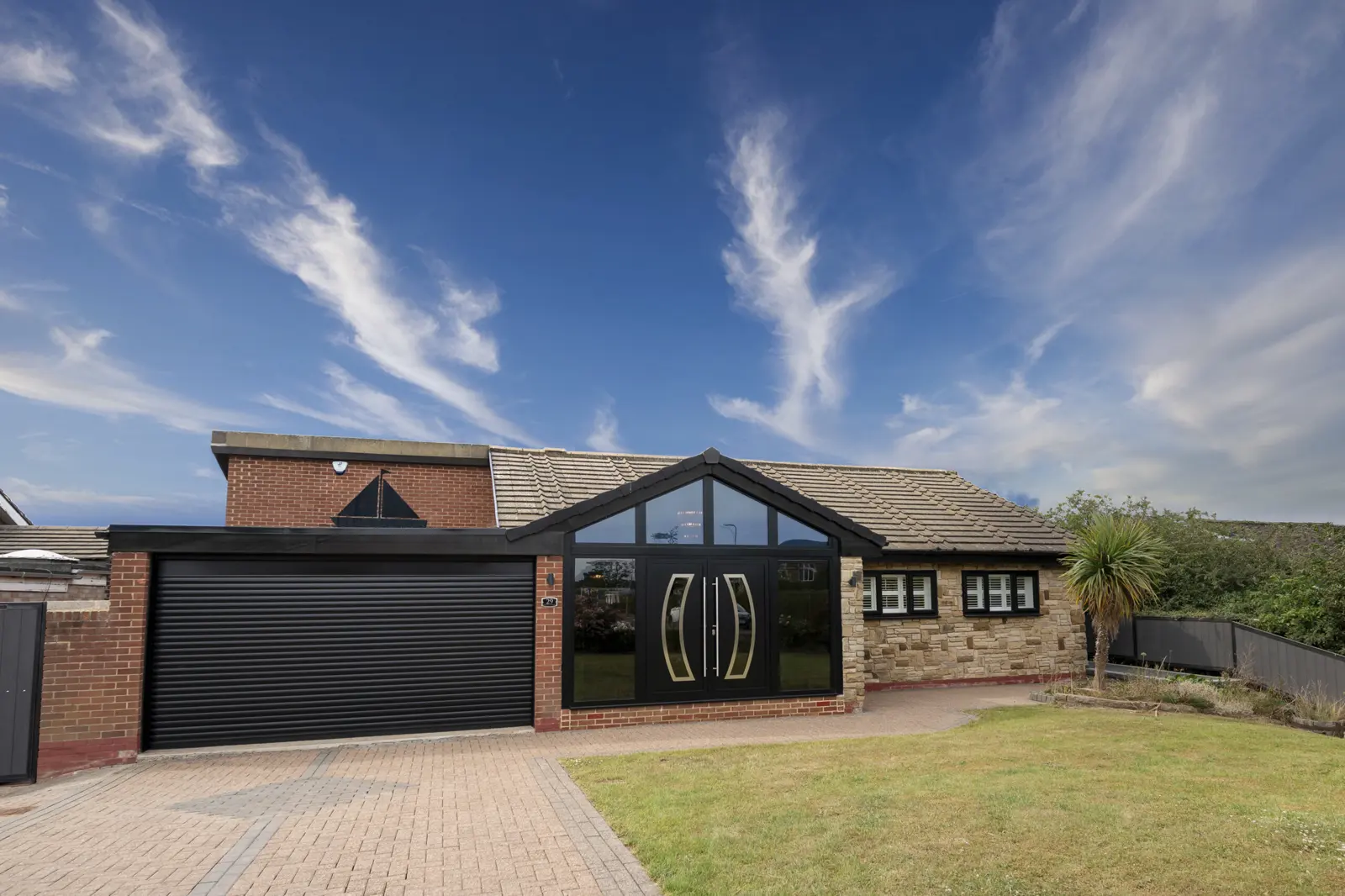 A single-storey red brick and stone bungalow with a grey tiled roof, a black roller garage door, and a paved drive. The Green, Thornaby.